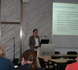  Referentin spricht am Pult und schaut zu den Teilnehmern