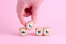 Eine Hand stellt einen W&uuml;rfel mit einem Rolli drauf zwischen andere W&uuml;rfel, die Menschen zeigen.