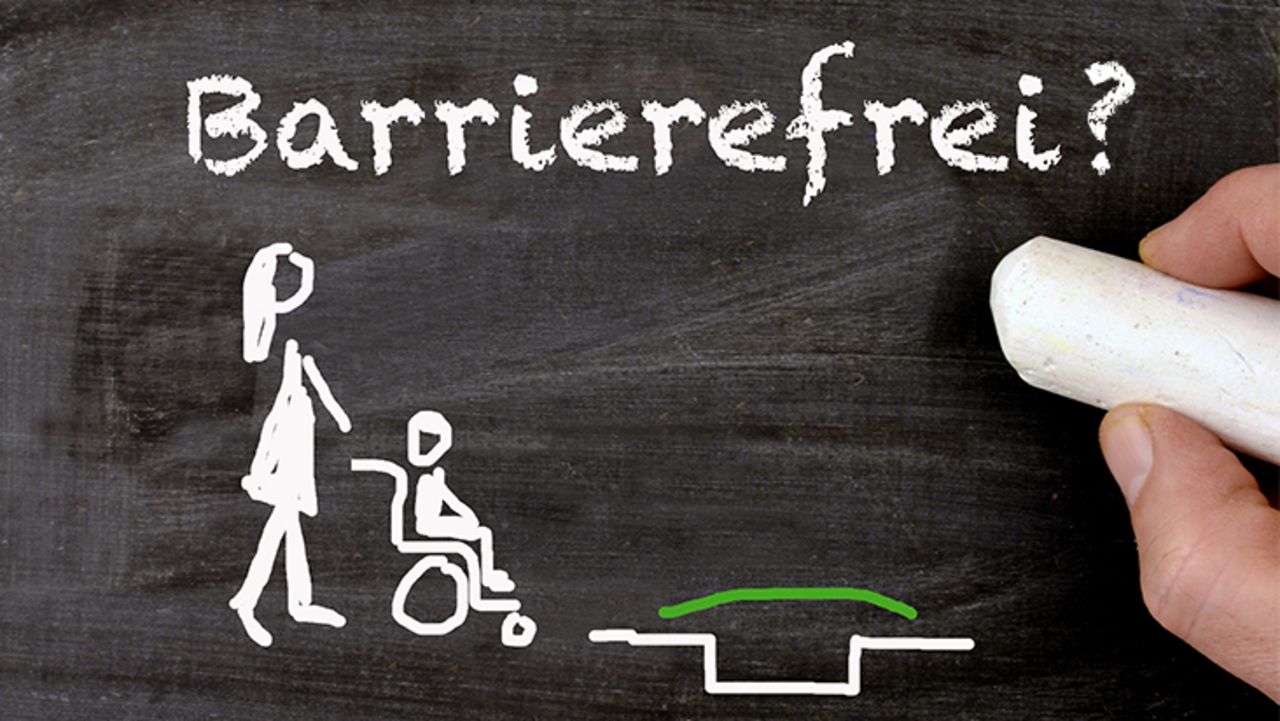 Auf einer Tafel malt eine Hand mit Kreide ein Kind im Rollstuhl, die von einer Person auf eine Grube zugeschoben wird. Darüber steht: Barrierefreiheit?!