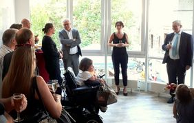 Menschen im Halbkreis als Zuhörer und vorne eine Frau die eine Rede hält