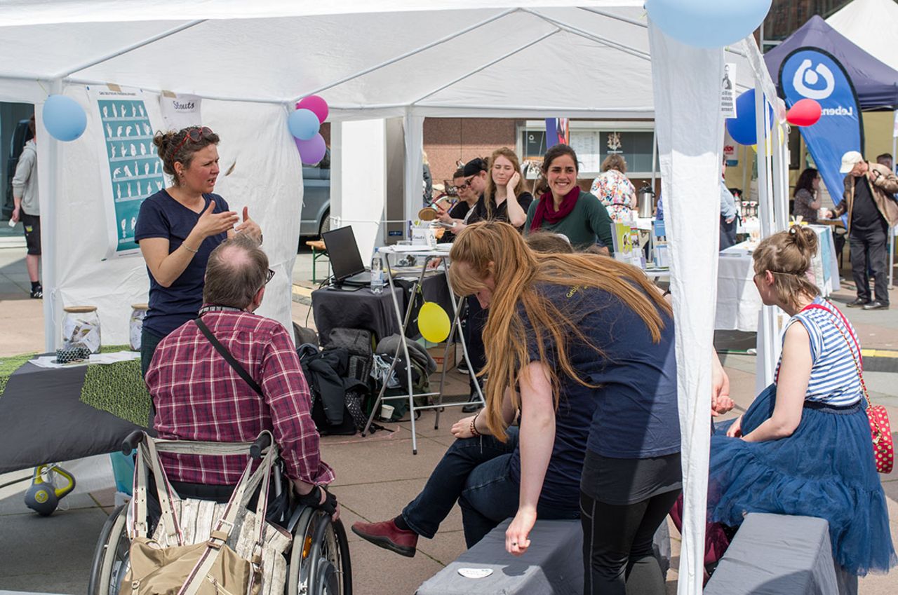 Eine Frau steht unter einem Pavillon und gibt den Besucher*innen einen Schnupperkurs in Gebärdensprache.