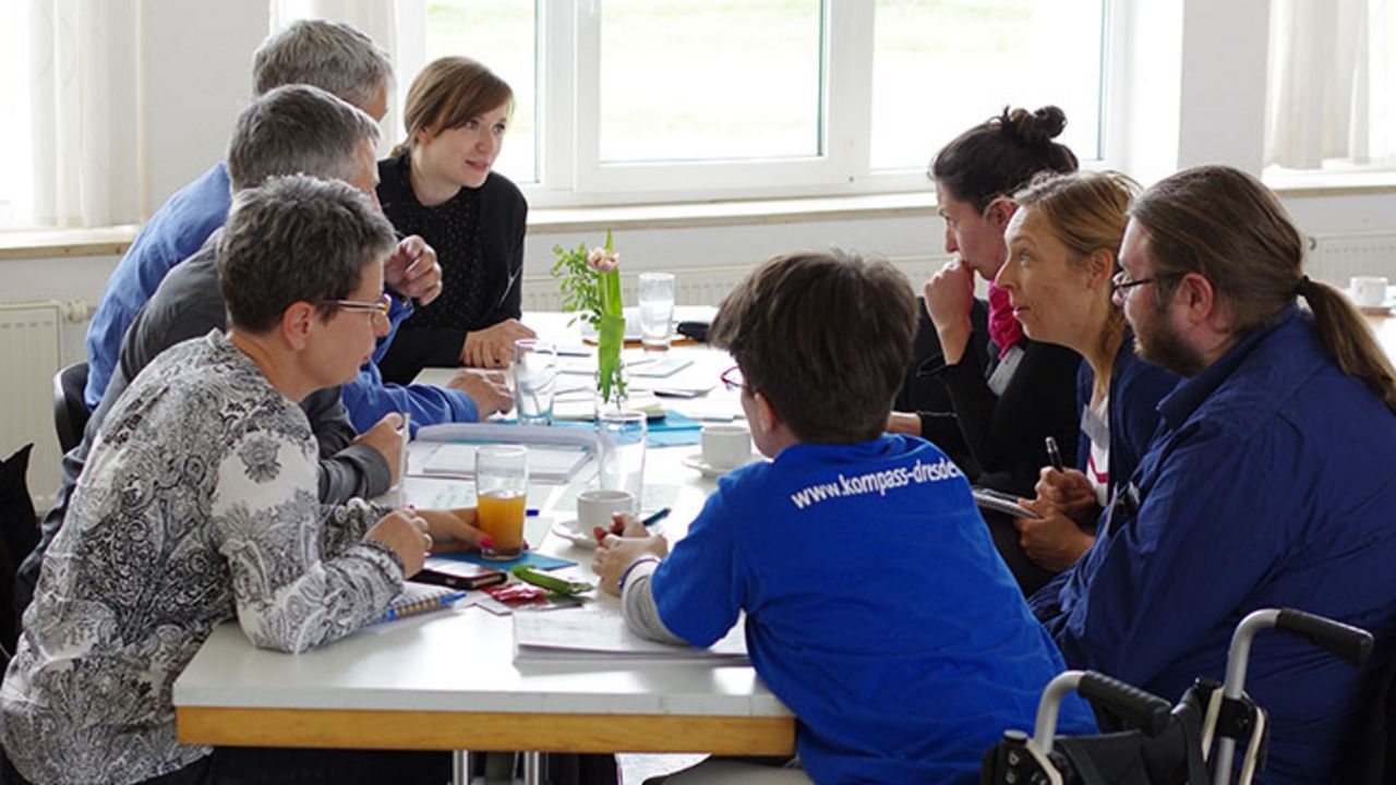 Viele Personen sitzen an einem Tisch bei einer Netzwerkveranstaltung und reden vertieft miteinander.