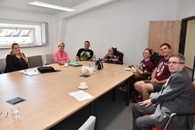 Blick auf Tisch mit sitzenden Teilnehmern, sie blicken in die Kamera