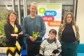 Simone Fass, Birger H&ouml;hn und Marsha Richarz stehen vor einem Roll-Up, auf dem "Weil Vielfalt fetzt" steht. Judith H&ouml;hne sitzt in ihrem Rollstuhl zwischen ihnen. 