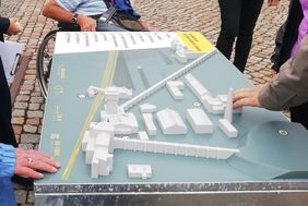 Ein Tastmodell des Bergbaumuseums. Es stehen Menschen um das Modell herum und drei H&auml;nde betasten es vorsichtig