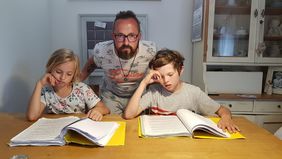 Vater mit zwei Kindenr am Tisch vor Schulbüchern und Heften