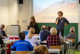 Christoph Marx redet am Mikrofon vor Teilnehmenden w&auml;hren Luise Jahn Lautsprecher aufbaut