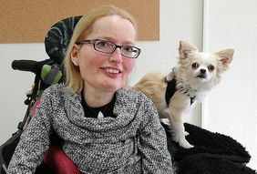 lächelnde Frau mit blonden Haaren und Brille plus kleinem Hund auf der Schulter