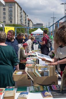 St&auml;nde mit Infomaterialien und B&uuml;chern. Viele Menschen stehen an den Tischen und begutachten das Angebot.
