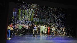 Viele junge Menschen stehen auf einer Theaterb&uuml;hne. Die Scheinwerfer leuchten hell und hinter der Gruppe steht sehr gro&szlig; Unart an der Wand. Einige tragen Kost&uuml;me, andere haben sich einfach schick gemacht. Einzelheiten lassen sich schlecht erkennen. Die Jugendlichen stehen in einem bunten Konfettiregen. Er regnet von oben auf B&uuml;hne herab. Alle freuen sich. Viele von ihnen klatschen in die H&auml;nde. Es ist der Abschluss des Unart-Finale 2022 im Kleinen Haus. 