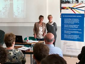 zwei Frauen im Publikum vor Leinwand und Rollup