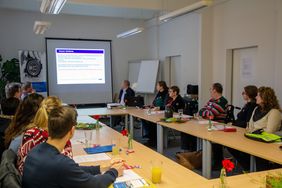 Teilnehmern sitzen in U-Form am Tisch und hören zu