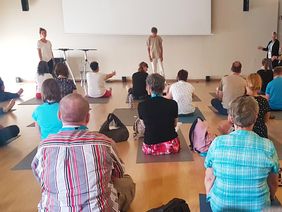 Kursteilnehmer sitzen auf ihren Matten vor dem Yoga-Lehrer Tobias eber