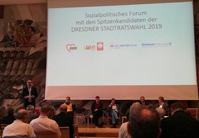 Blick auf B&uuml;hne mit Modertor und Podiumsg&auml;sten